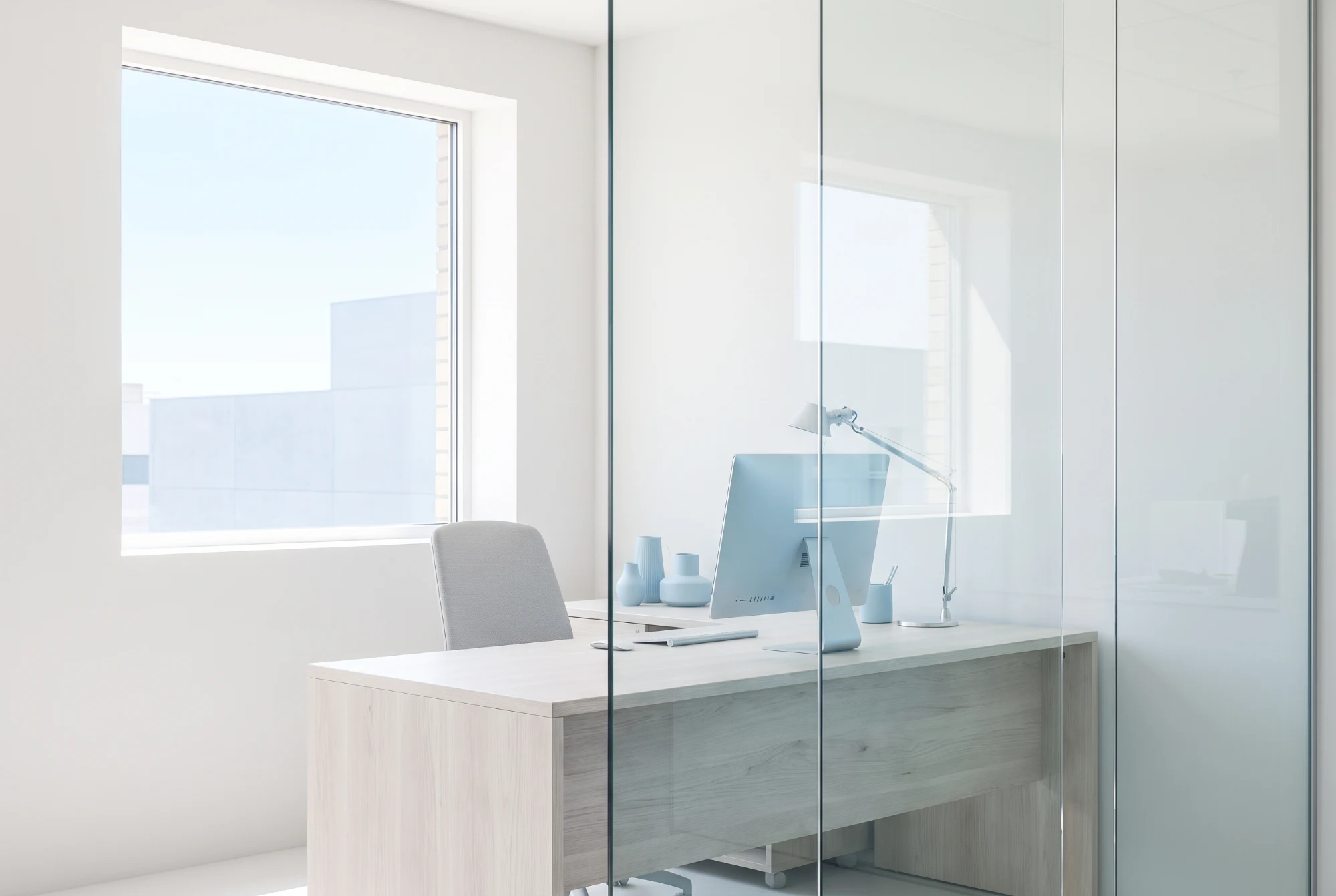 Pale desk and slim monitor behind a glass partition in daylight