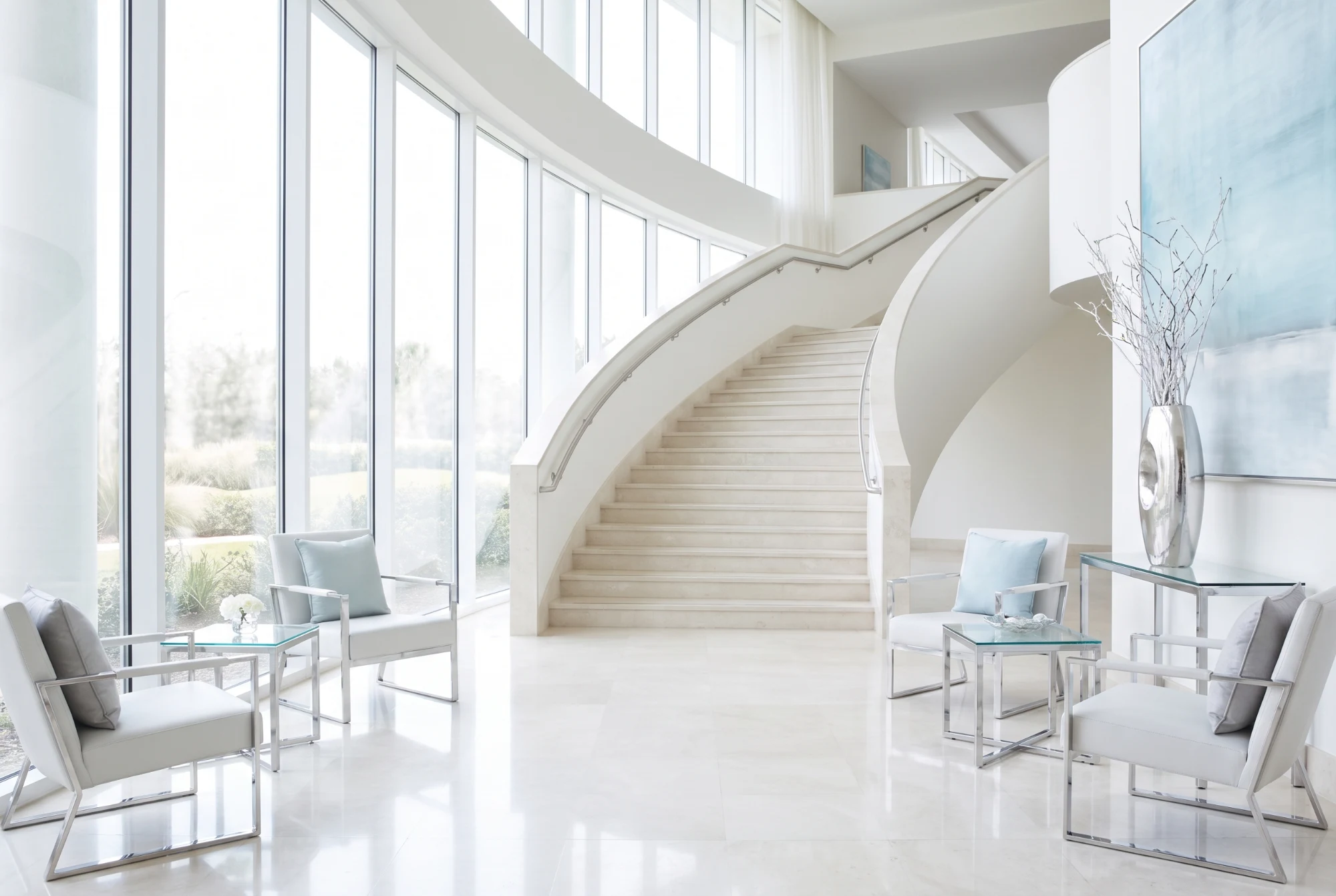 Bright hotel lobby with a light curved staircase and tall windows