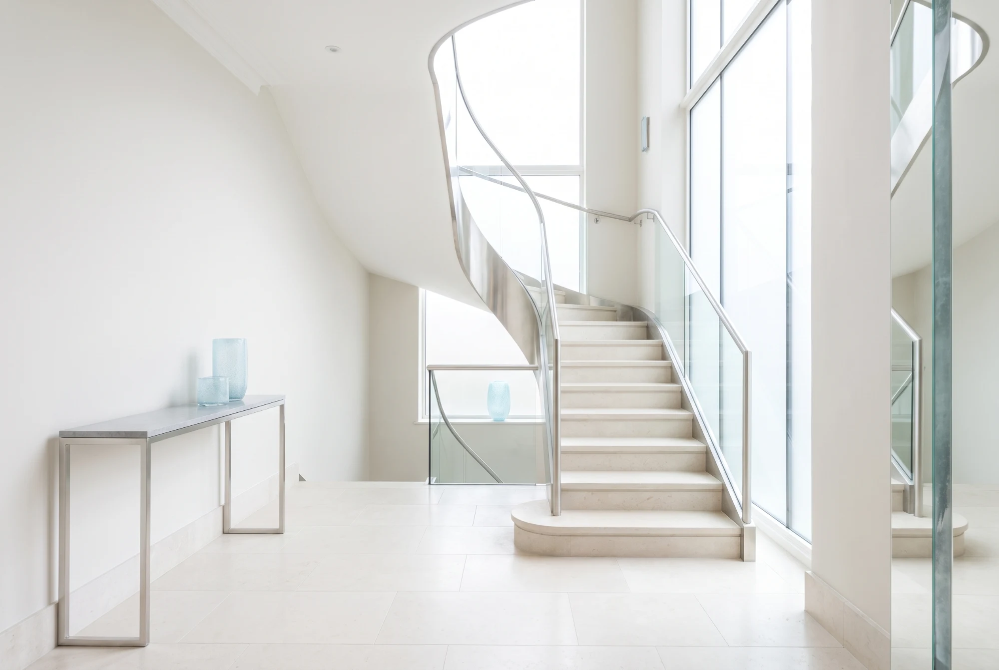 Pale limestone entrance hall with a light staircase and a plain console table
